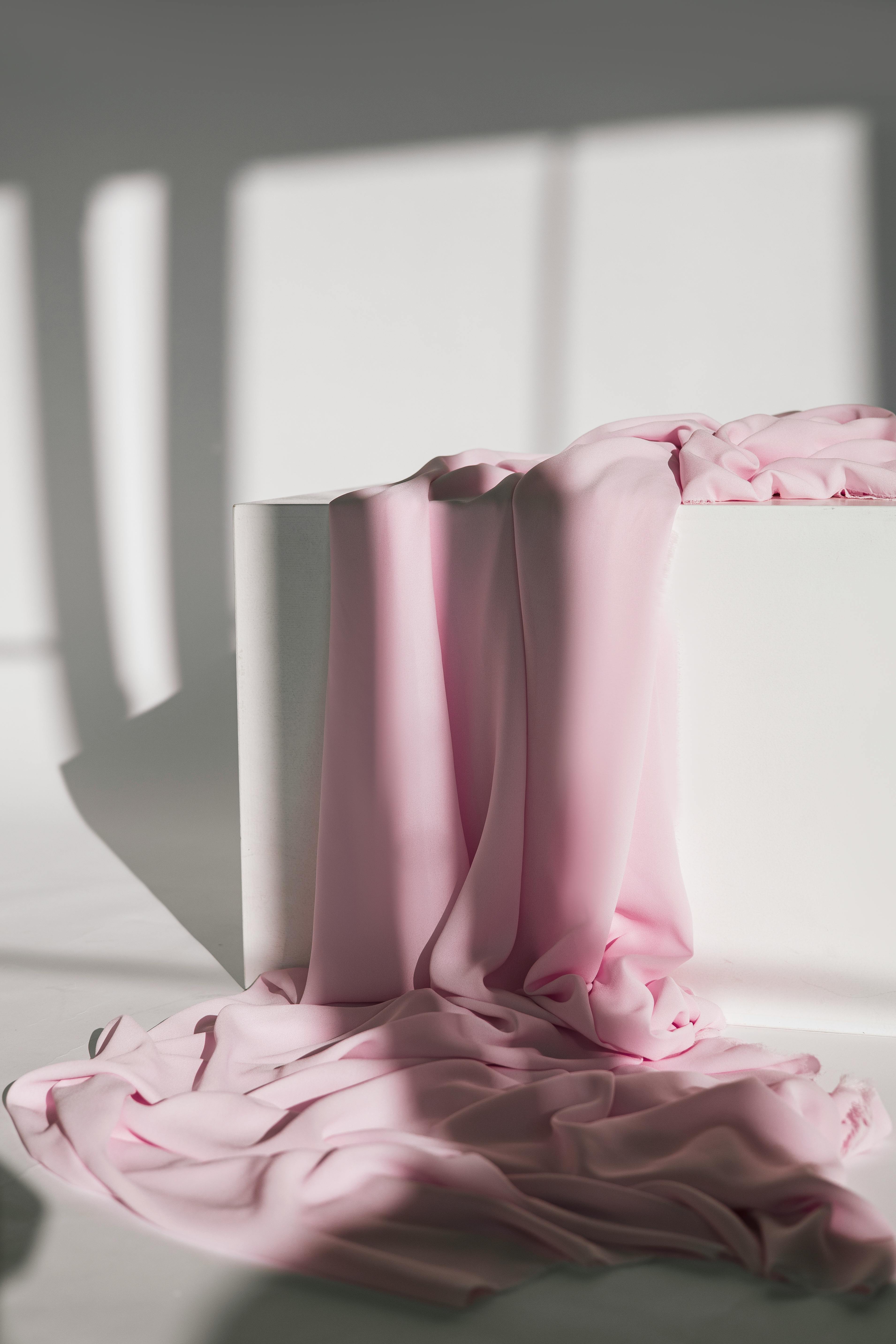 Pink fabric draped over a white surface with soft shadows