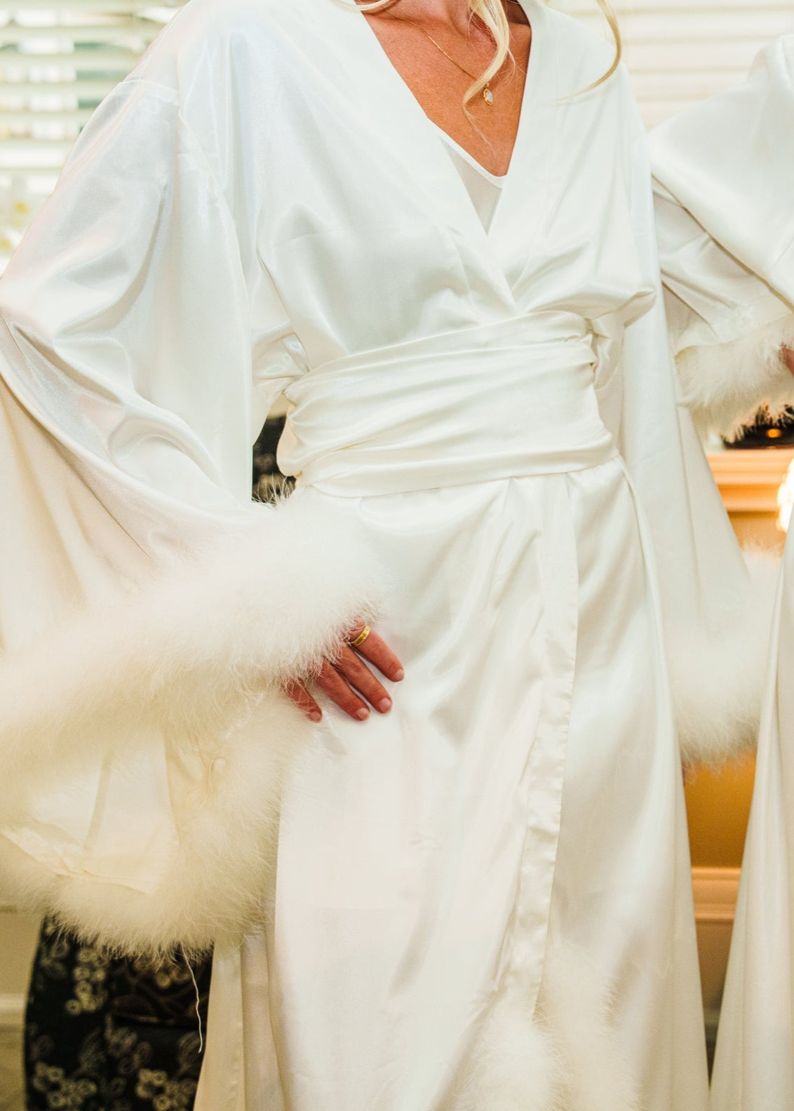 Two women in white satin robes with fur cuffs standing next to each other.