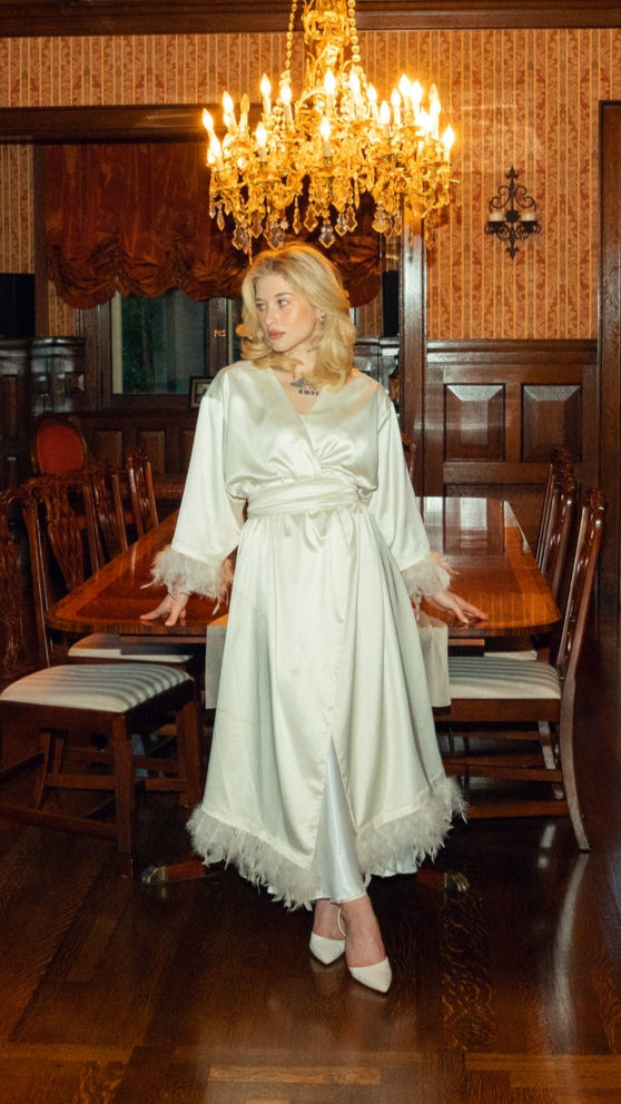 Woman in a white dress standing in a room with wooden paneling and a chandelier.