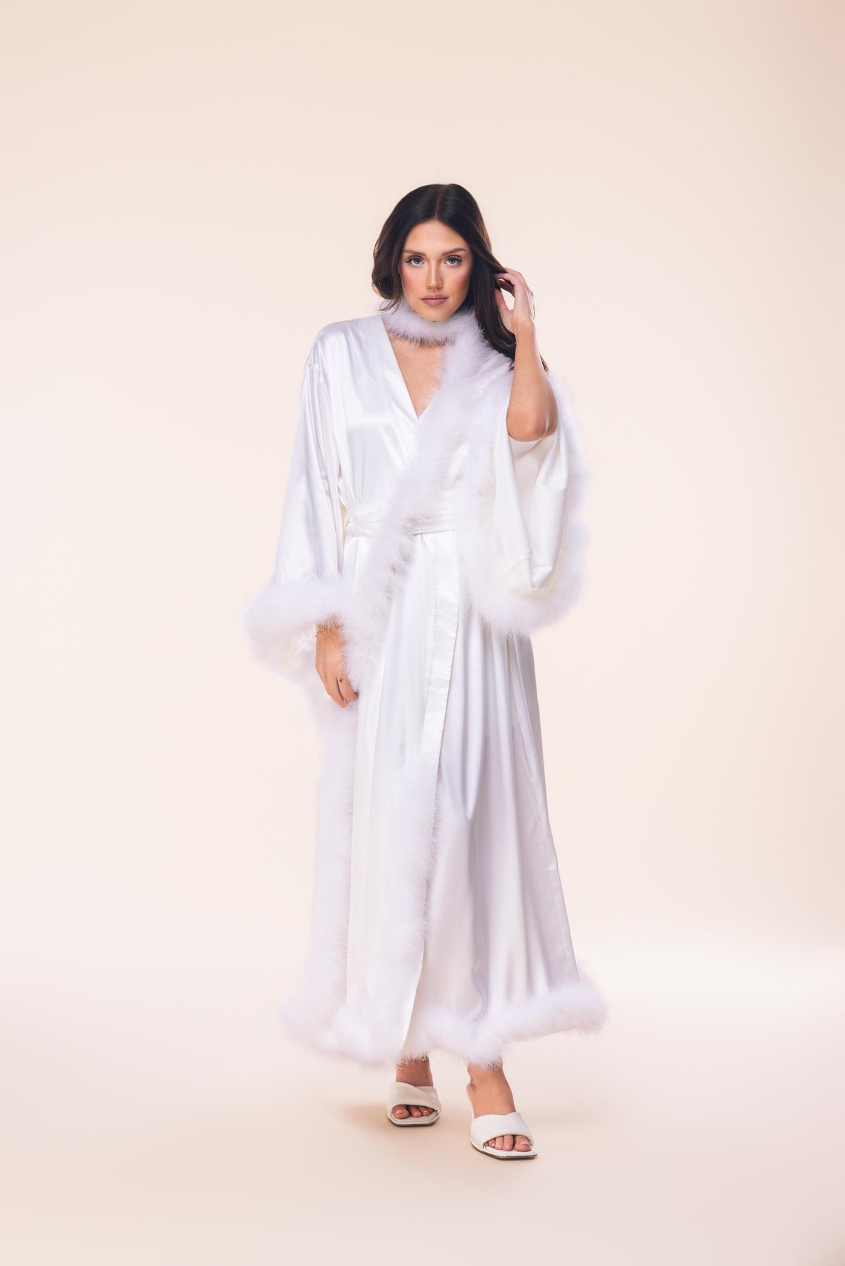 Woman wearing a white dress with sheer sleeves against a beige background