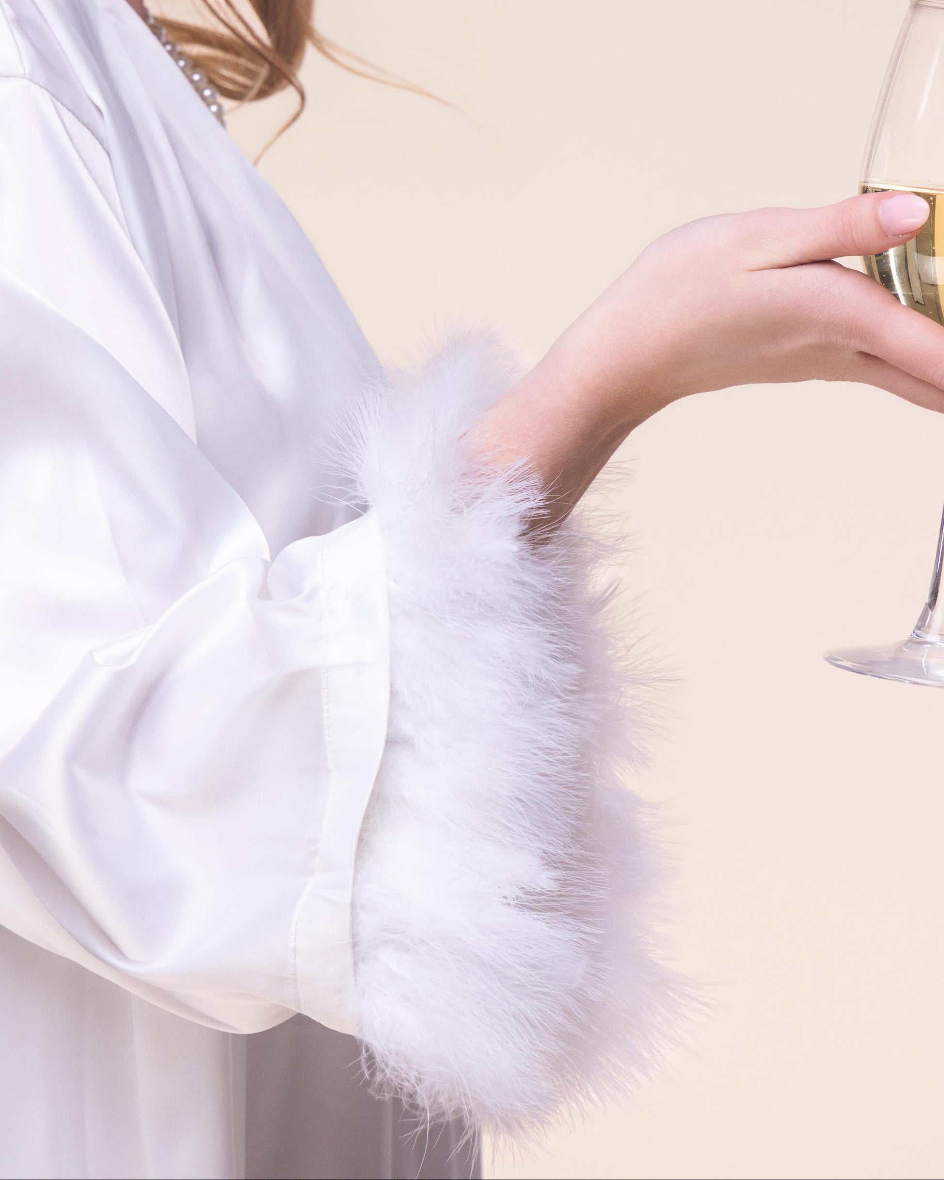 Woman in a white robe holding a glass of white wine against a beige background